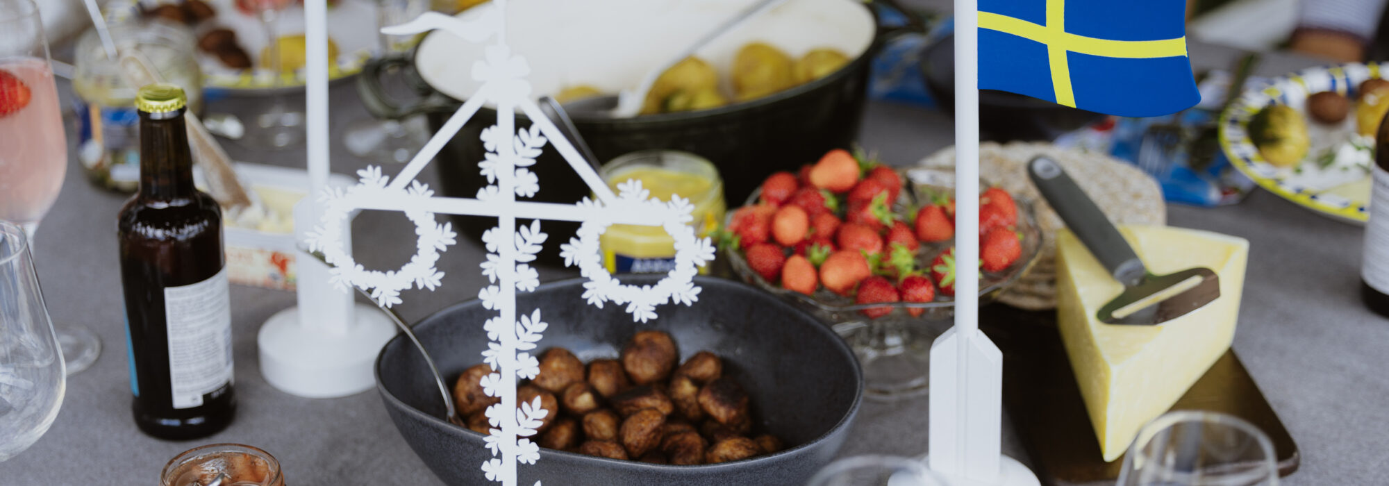 En grupp människor som sitter runt ett bord med mat midsommarmat.